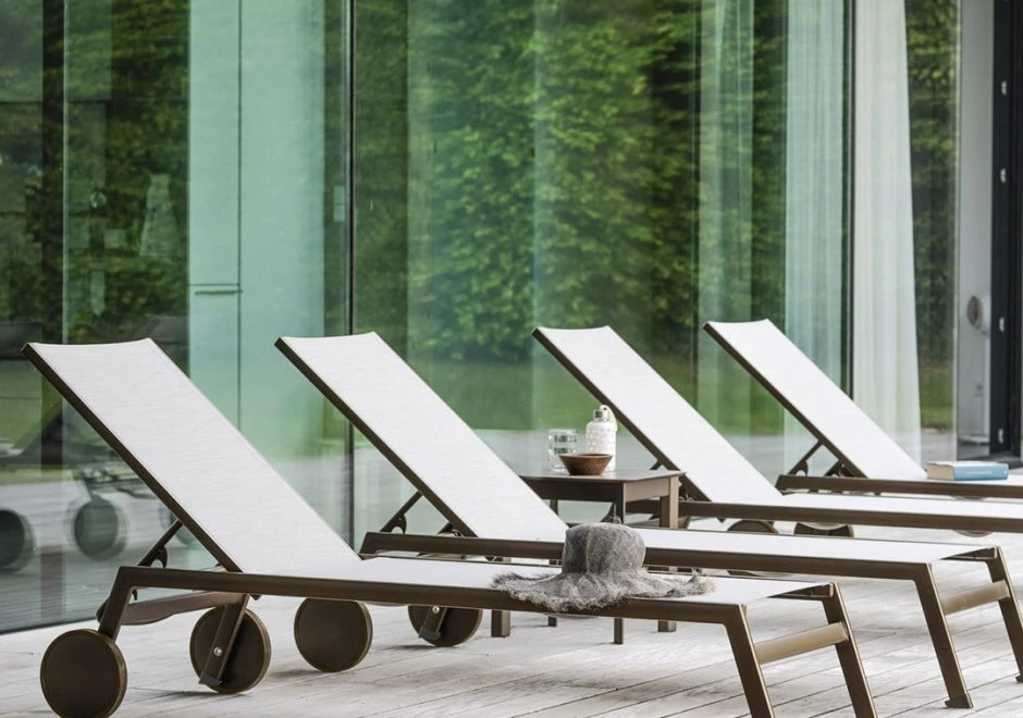 Quatro chaise longue com estrutura de alumínio, assento e encosto em PVC branco, visto de lado em uma area externa.