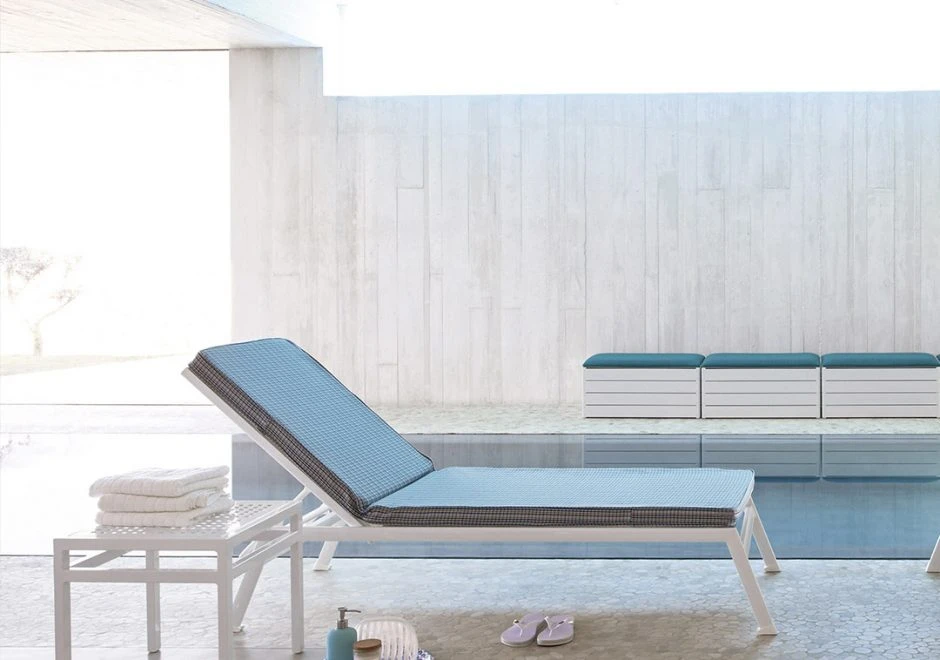 Chaise longue com estrutura de alumínio, assento e encosto em PVC cinza, visto de lado em uma area externa.