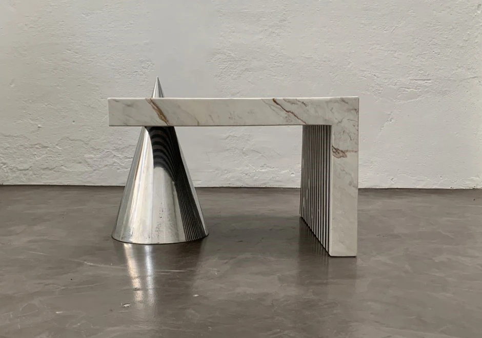 Vista lateral da mesa, mostrando a combinação entre o tampo de mármore preto e a base cônica em alumínio.