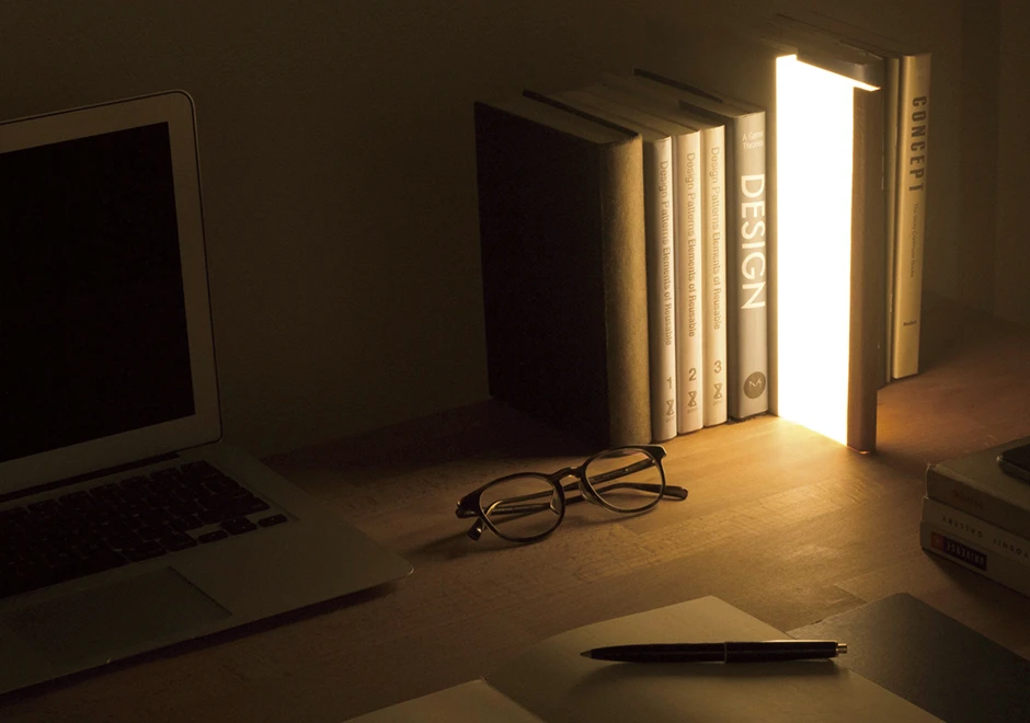 Vista lateral da luminária de mesa Night Book, mostrando a luminária em posição vertical emitindo luz.