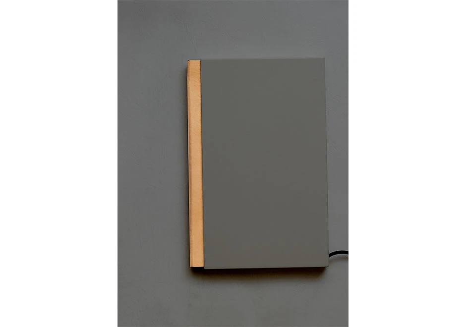 Vista frontal da luminária de mesa Night Book, destacando a estrutura em aço e acrílico com capa de couro cinza.