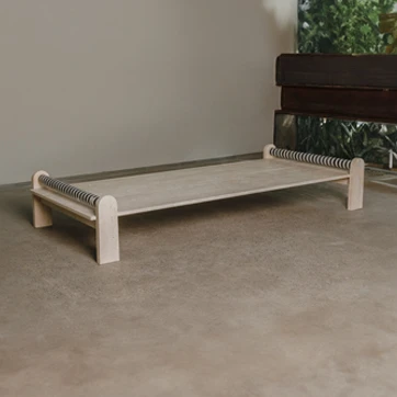 Vista lateral da mesa de centro farol em fundo branco, que realça a espessura do tampo em mármore e a estrutura em Travertino Romano Bruto.