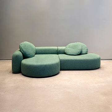 Sofá modular branco com pés de madeira, almofadas de assento e encosto fixas e duas almofadas decorativas, visto de lado em um fundo transparente.