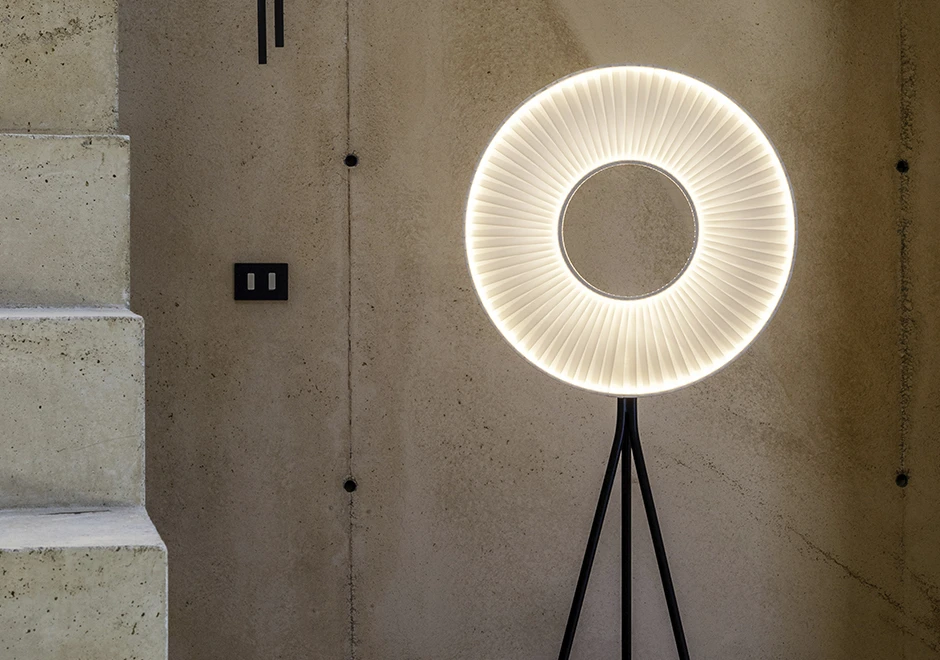 Luminária de chão Iris da DCW Éditions em um ambiente minimalista com parede de concreto aparente e design moderno.