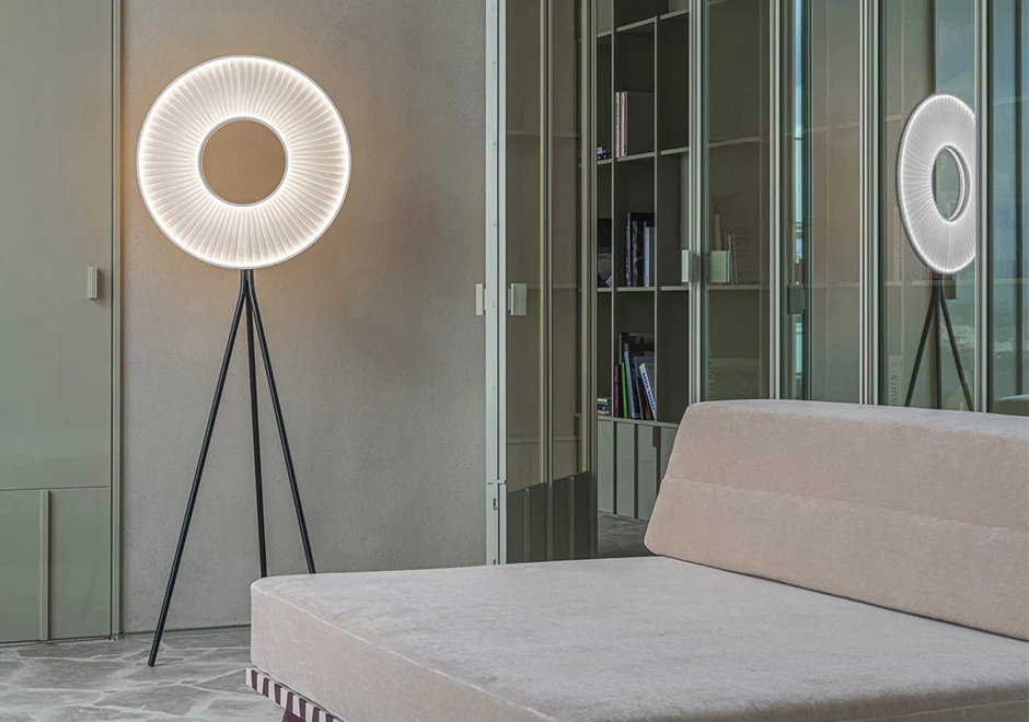 Luminária de chão Iris da DCW Éditions com iluminação circular, destacada em uma sala moderna com sofá bege