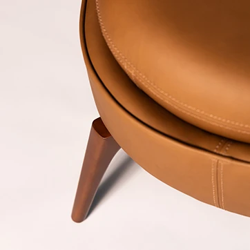 Detalhe da poltrona Bromélia, mostrando estofado em couro caramelo e pés de madeira maciça, destacando o acabamento sofisticado e artesanal