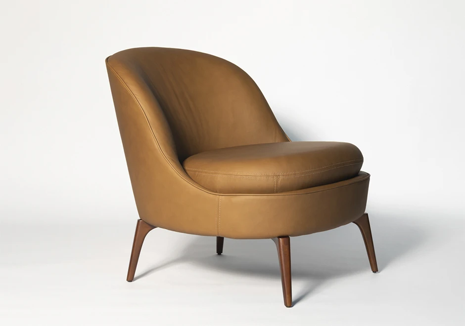 Poltrona Bromélia em couro caramelo e pés de madeira maciça, exibindo um design sofisticado com curvas suaves e estofado confortável