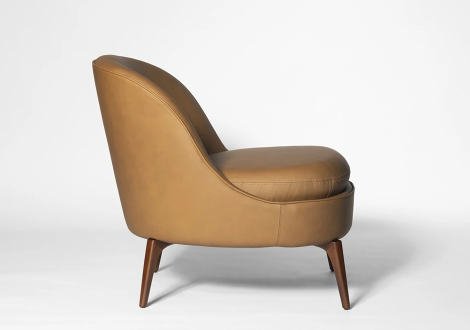 Vista lateral da Poltrona Bromélia em couro caramelo com pés de madeira maciça, destacando seu design ergonômico e estofado sofisticado.