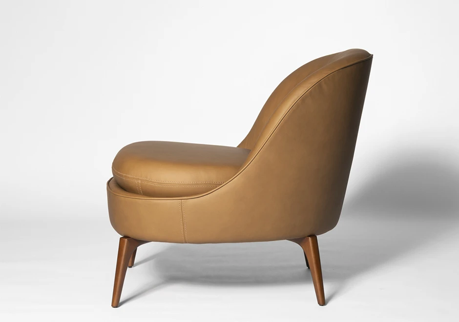 Vista lateral da Poltrona Bromélia em couro caramelo, evidenciando seu design ergonômico, costura refinada e pés em madeira maciça para um toque sofisticado.