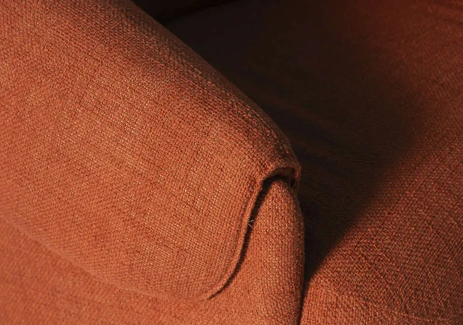 Detalhe do braço da poltrona Orca, evidenciando o tecido texturizado em tom terracota e o acabamento macio que reforça o conforto do design.