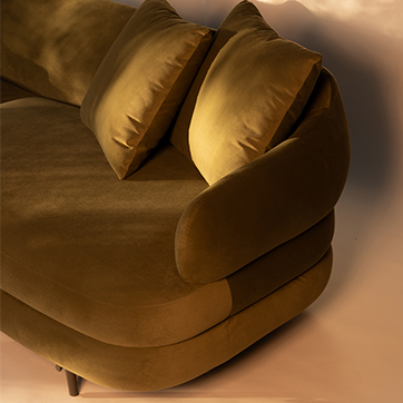 Detalhe do sofá Gaudi com encosto curvo e almofadas macias, destacando o conforto e a sofisticação do estofamento aveludado.