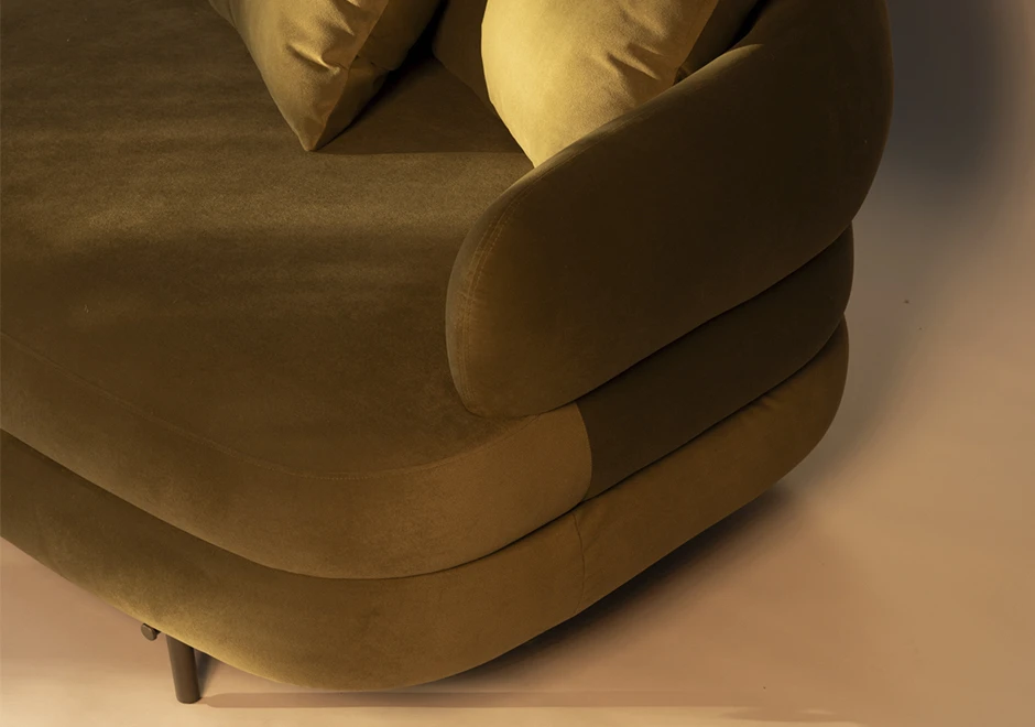 Detalhe do braço do sofá Gaudi, com estofamento aveludado verde, curvas sofisticadas e acabamento impecável, evidenciando seu design aconchegante.