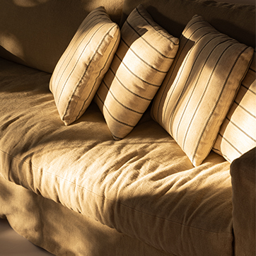 Detalhe do sofá Julia da Firma Casa, com almofadas confortáveis e tecido sofisticado, destacando aconchego e elegância.