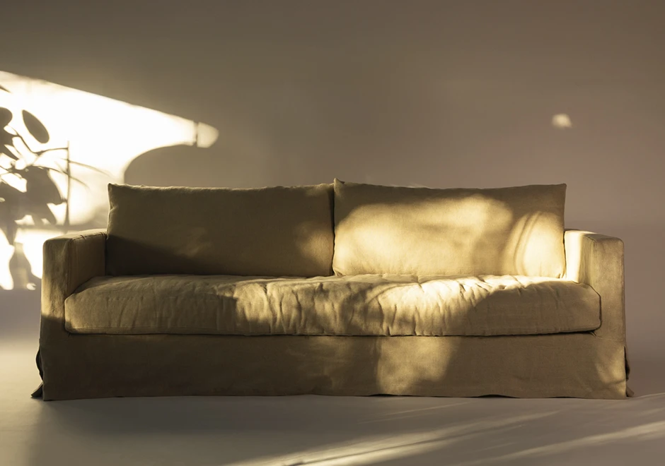 Sofá Julia da Firma Casa, estofado em linho e com design aconchegante, realçado pela luz natural do ambiente.